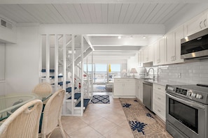 A modern kitchen with white cabinetry, a built-in oven, and a glass dining table with wicker chairs. - Ocean Colony-Enjoy Ocean Views at this beautiful Condo! (Ocean City)