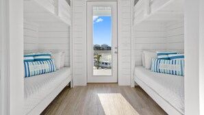 A narrow hallway with a white door leading to a balcony. The room has a white bed with striped pillows and a white headboard.