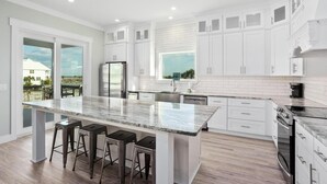 A modern kitchen with white cabinets, a granite island with bar stools, and a large window offering a view of the outdoors.