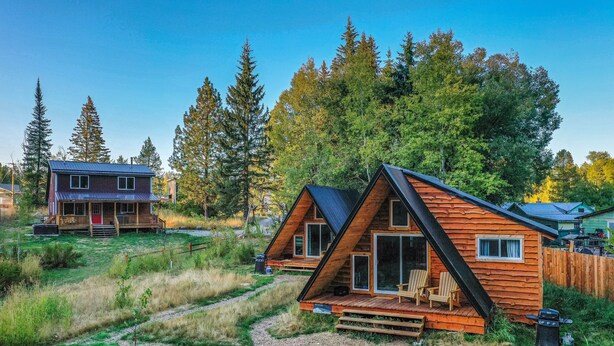 Una cabaña con terraza y porche cubierto, rodeada de un bosque.
