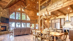 A spacious living area with a fireplace, wooden floors, a large sofa, and a dining area with wooden chairs and a table. - Newly Built 2021!! 4 BD 4.5 BA, Luxury Home, Mtn Views, Hot-tub! (Maggie Valley)