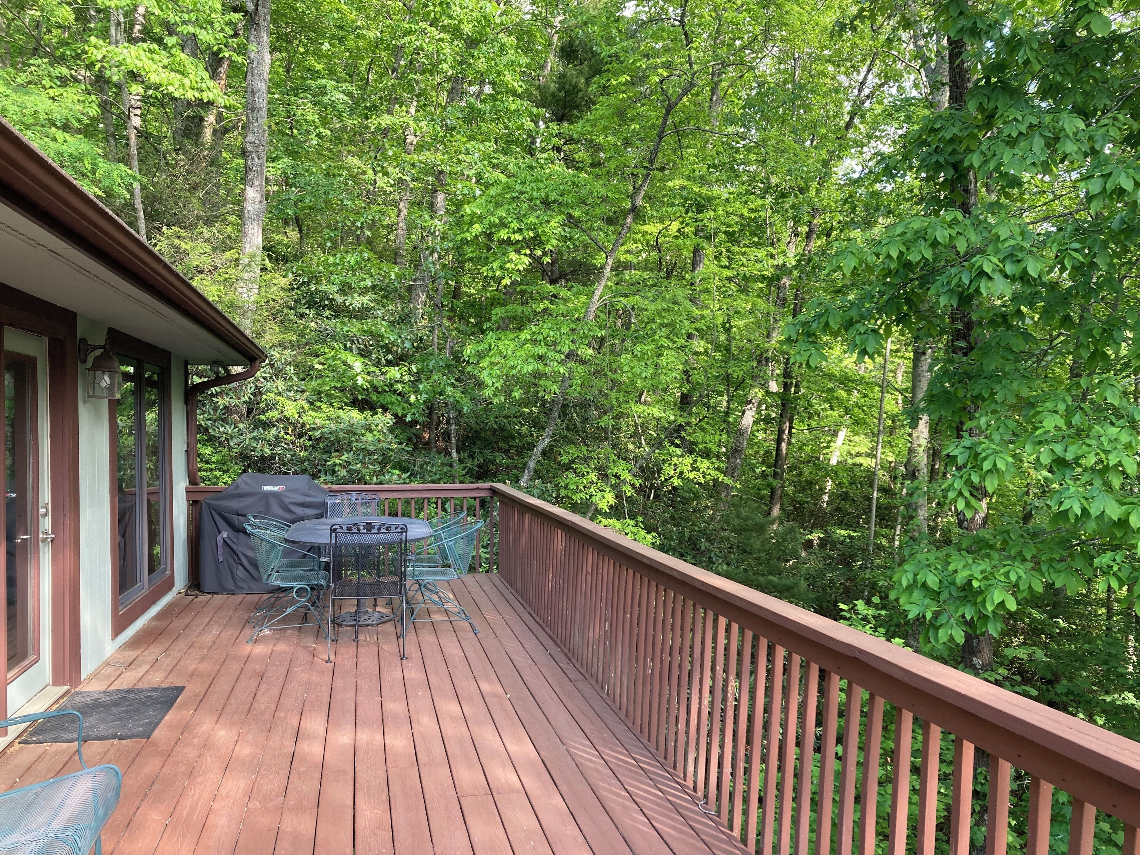 Une terrasse en bois avec une table et des chaises, entourée d’une forêt dense.
