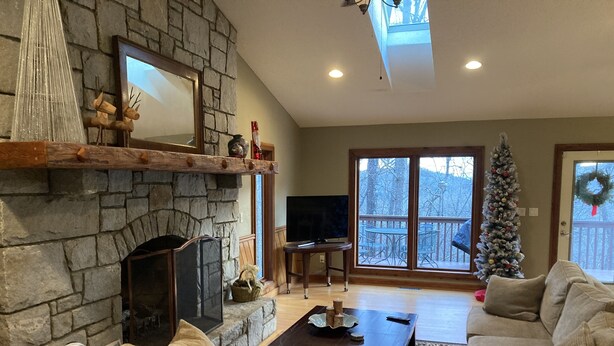 A cozy living room with a stone fireplace, a television, and a Christmas tree. - Romantic Mountain house with views (Fairview)