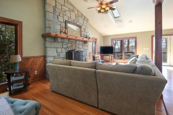 A cozy living room with a stone fireplace, a large sectional sofa, and a flat-screen TV.