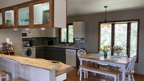 A modern kitchen with wooden cabinets, a dining area with a wooden table and chairs, and large windows providing natural light. - Romantic Mountain house with views (Fairview)
