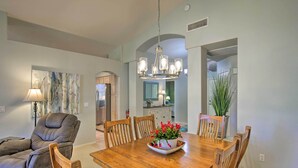 A dining area with a wooden table, six chairs, a chandelier, and a potted plant. - Snowbird & Golfer Oasis! Lake-View Peoria Retreat (Surprise)