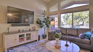 A living room with a TV, a sofa, a coffee table, and a large window. - Snowbird & Golfer Oasis! Lake-View Peoria Retreat (Surprise)