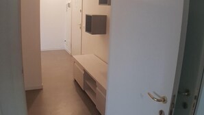 Ein schmales Gang mit einer weißen Tür rechts, einer Bank und einem an der Wand befestigten Schrank.