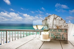 Ein Holztisch mit zwei Gläsern Weißwein, einer Kerze und einem Schild mit der Aufschrift 'YOU, ME, & THE BEACH'.