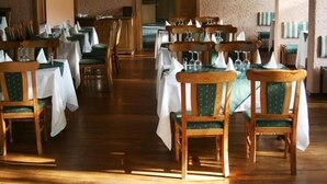 A restaurant with wooden tables and chairs, white tablecloths, and green cushioned chairs.