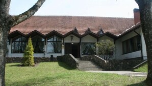 A two-story building with a red-tiled roof, a stone staircase leading to the entrance, and a small lawn area.