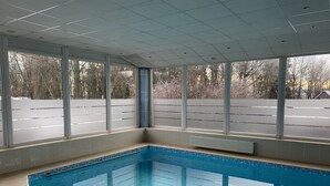 A swimming pool with clear blue water, surrounded by large windows offering views of a snowy landscape.