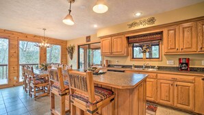 A spacious kitchen with wooden cabinets, a large island, and a dining area with chairs and a table. - Fire Pit + Views: Family Cabin on Table Rock Lake (Golden)