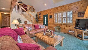 A cozy living room with a leather sofa, a wooden coffee table, a TV, and a staircase leading to an upper level. - Fire Pit + Views: Family Cabin on Table Rock Lake (Golden)