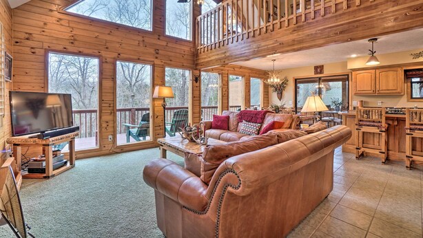 A spacious living room with a large leather sofa, wooden flooring, and a television on a stand. - Fire Pit + Views: Family Cabin on Table Rock Lake (Golden)
