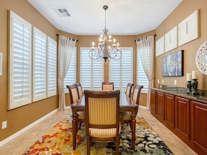 A dining area with a chandelier, a large table, chairs, and a patterned rug.