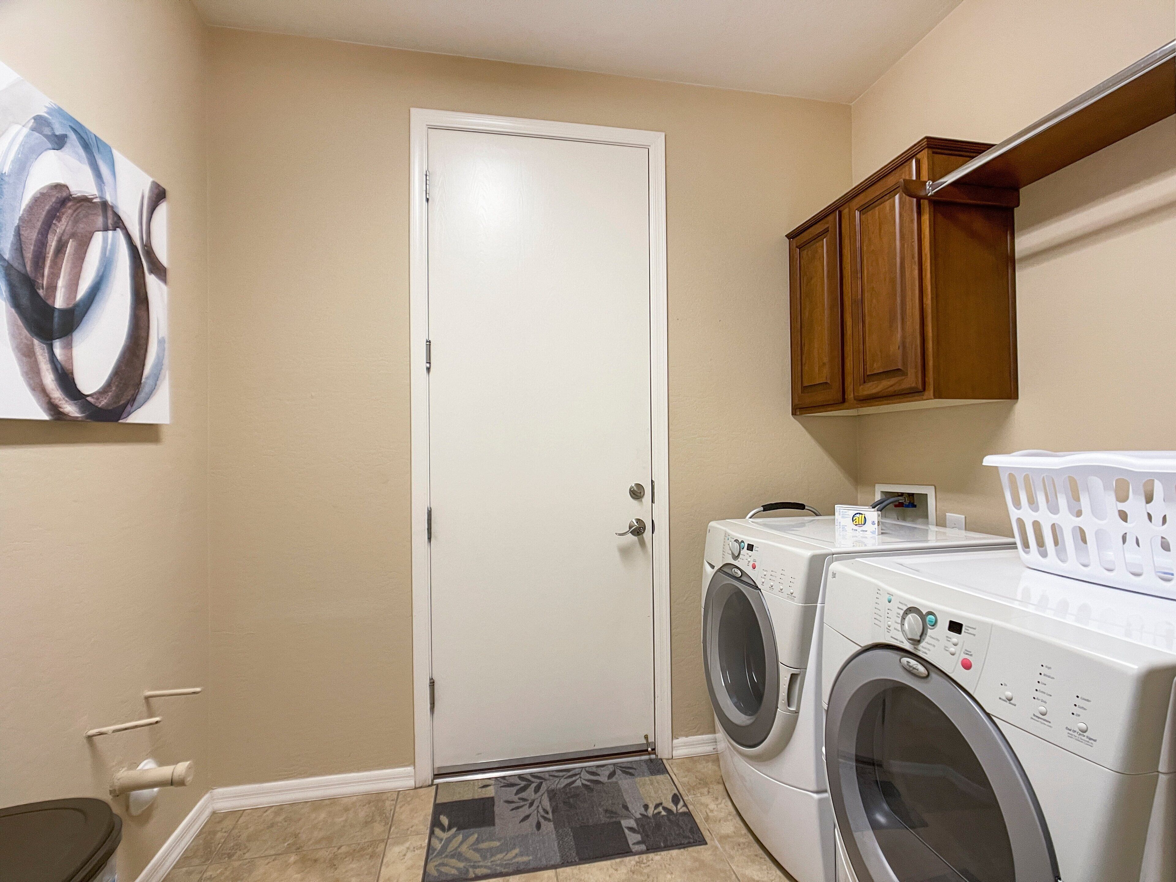 A laundry room with a door, two washing machines, a basket, and wooden cabinets.
