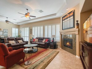 A spacious living room with a fireplace, leather sofas, a round coffee table, and a ceiling fan.