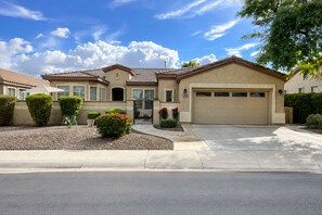 A residential house with a garage, a driveway, and a well-maintained front yard with shrubs and a small tree.