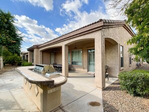 A house with a covered patio, outdoor seating, and a barbecue grill.