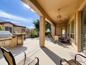 An outdoor patio with a grill, chairs, and a ceiling fan.