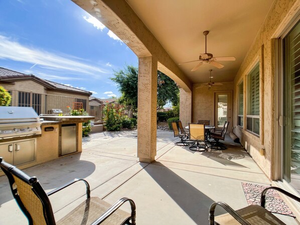 An outdoor patio with a grill, chairs, and a ceiling fan.