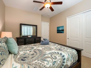 Une chambre à coucher avec un lit, une commode, un ventilateur de plafond et une porte.