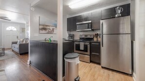 A modern kitchen with stainless steel appliances, a central island, and a grey sofa in the adjacent living area.