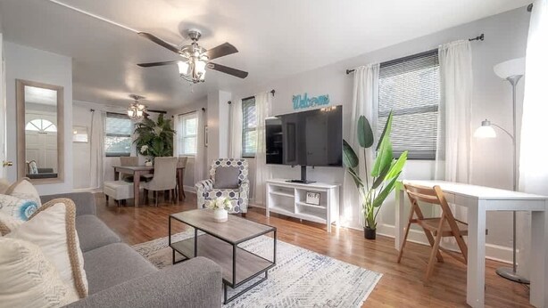 A modern living room with a sofa, coffee table, TV, and a dining area with chairs and a table.
