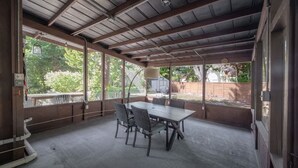 A covered outdoor patio with a table and chairs, large windows, and a view of the surrounding area.