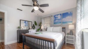 A bedroom with a bed, a ceiling fan, a nightstand, a lamp, and a window with blinds.