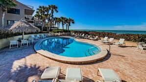 A pool area with lounge chairs, a thatched umbrella, and a view of the ocean.