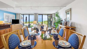 A dining area with a view of the ocean, a TV, and a plant.