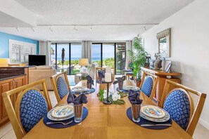 Un coin repas avec vue sur l’océan, une télévision et une plante.