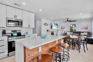 A modern kitchen with white cabinets, a stainless steel microwave, and a teal kettle.