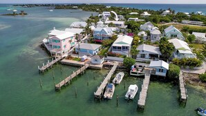 An aerial view of a coastal residential area with houses connected by docks to the water, boats moored at the docks, and a clear view of the ocean and distant islands. - Sea Merc: A Charming Haven with Captivating Views in Hope Town (Hope Town)