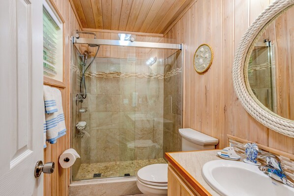 A wooden-paneled bathroom with a glass-enclosed shower, a toilet, and a sink with decorative items.