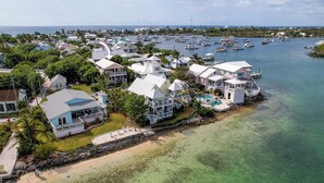 An aerial view of a coastal residential area with houses, a clear beach, and a marina with boats. - Sea Merc: A Charming Haven with Captivating Views in Hope Town (Hope Town)