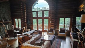A cozy log cabin interior with a large arched window, a fireplace, and a comfortable seating area. - Vinewood Estate Luxury Pool and Vineyard Retreat (Hillsboro)