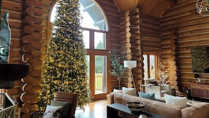 A log cabin interior with a large Christmas tree, a sofa, and a dining table. - Vinewood Estate Luxury Pool and Vineyard Retreat (Hillsboro)