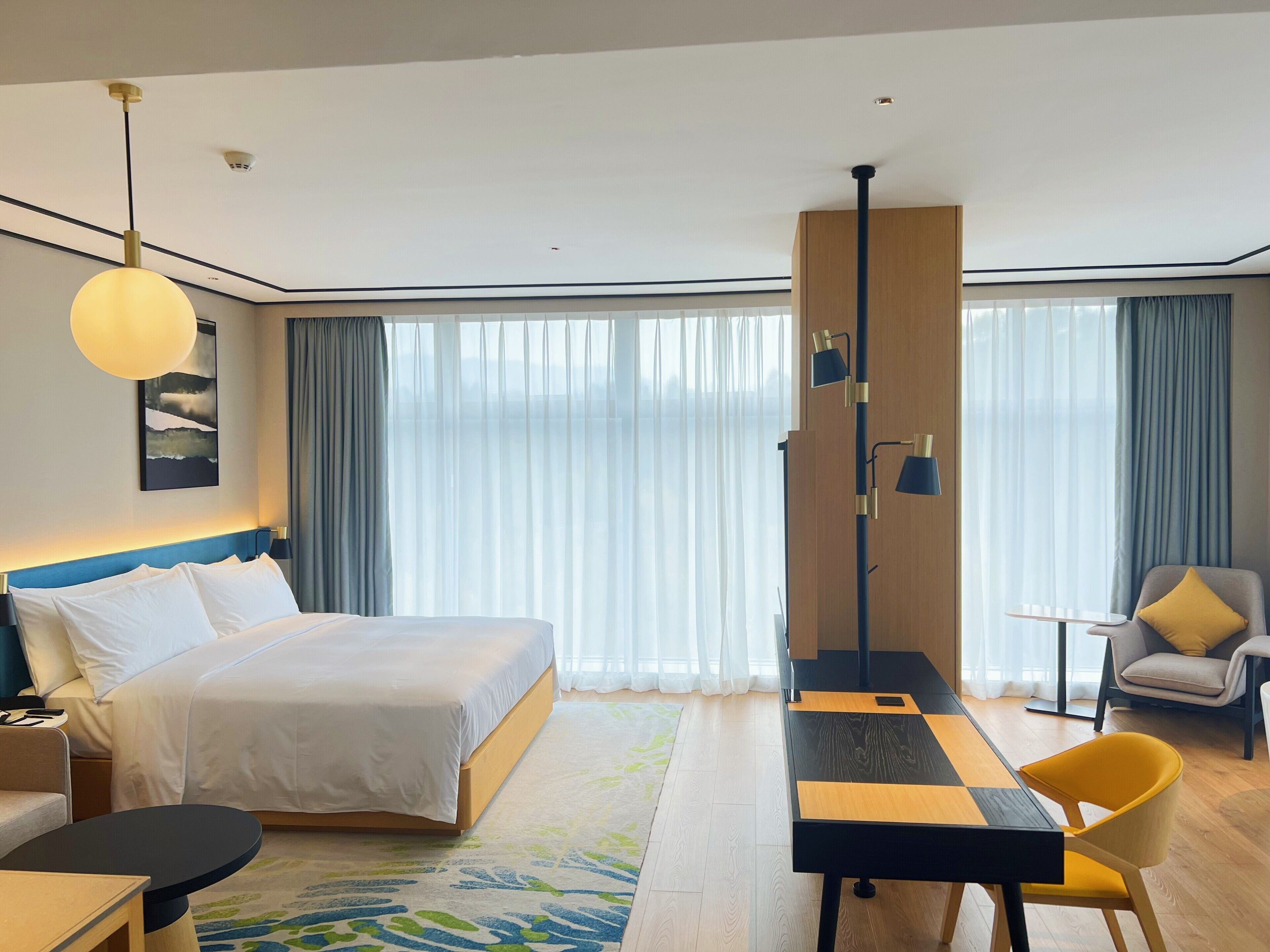 Una habitación de hotel moderna con una cama grande, un escritorio con silla, una mesita y un sofá.