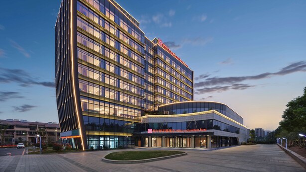 Un hôtel moderne à la façade incurvée, doté de plusieurs étages et arborant un logo bien visible sur le sommet.