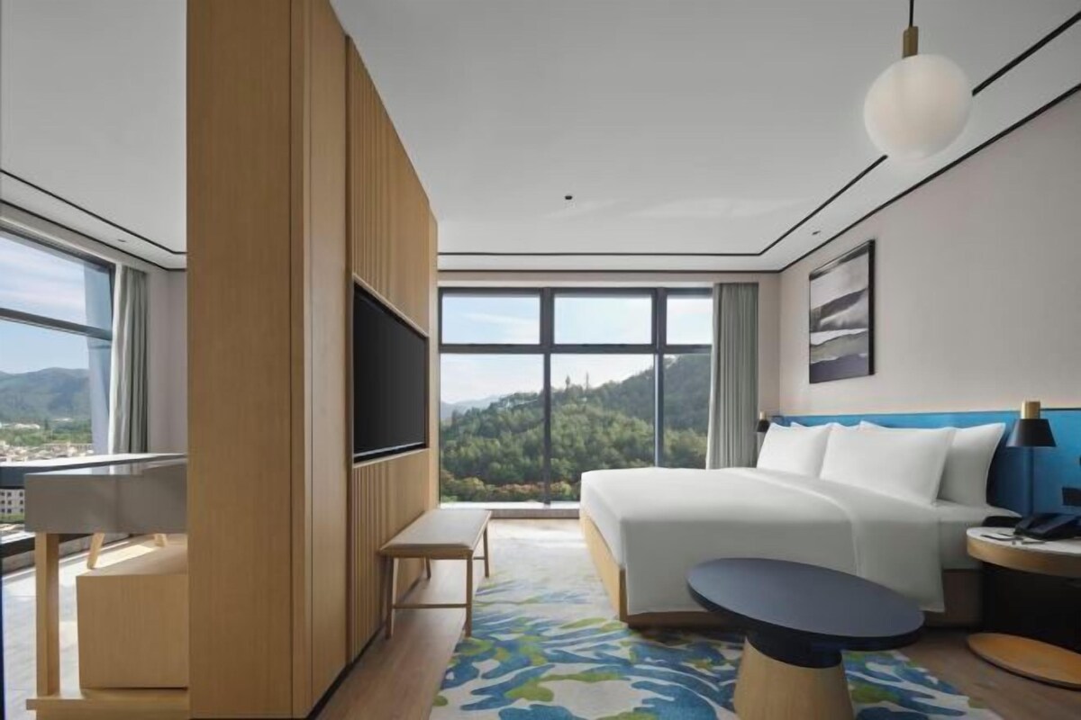 Habitación de hotel moderna con una cama grande, televisión, escritorio y vistas a las montañas.