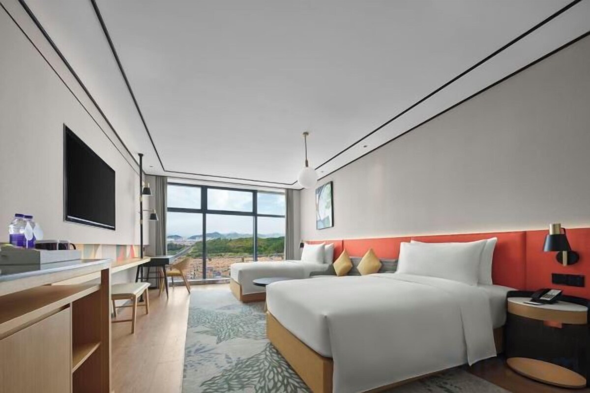 Ein modernes Hotelzimmer mit einem großen Bett, einem Schreibtisch, einem Fernseher und Blick ins Freie.