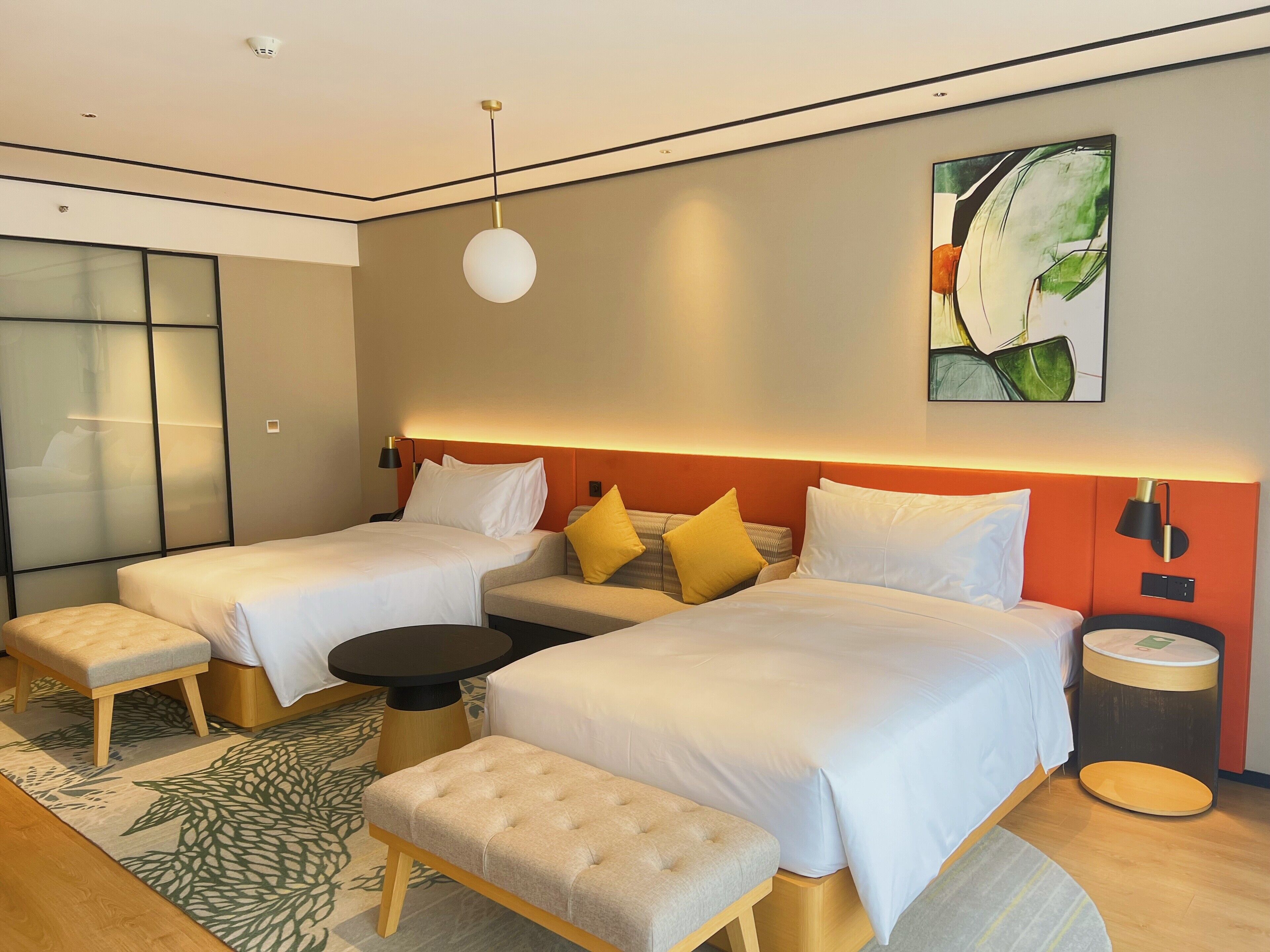 Et moderne hotelværelse med to senge, en bænk, et rundt bord og et stort vindue.
