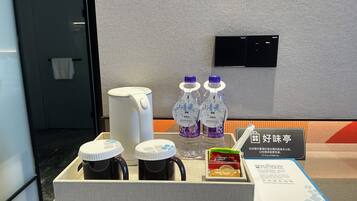 Zona de recepción de hotel con cafetera, dos botellas de agua, tetera y una pequeña caja de aperitivos.