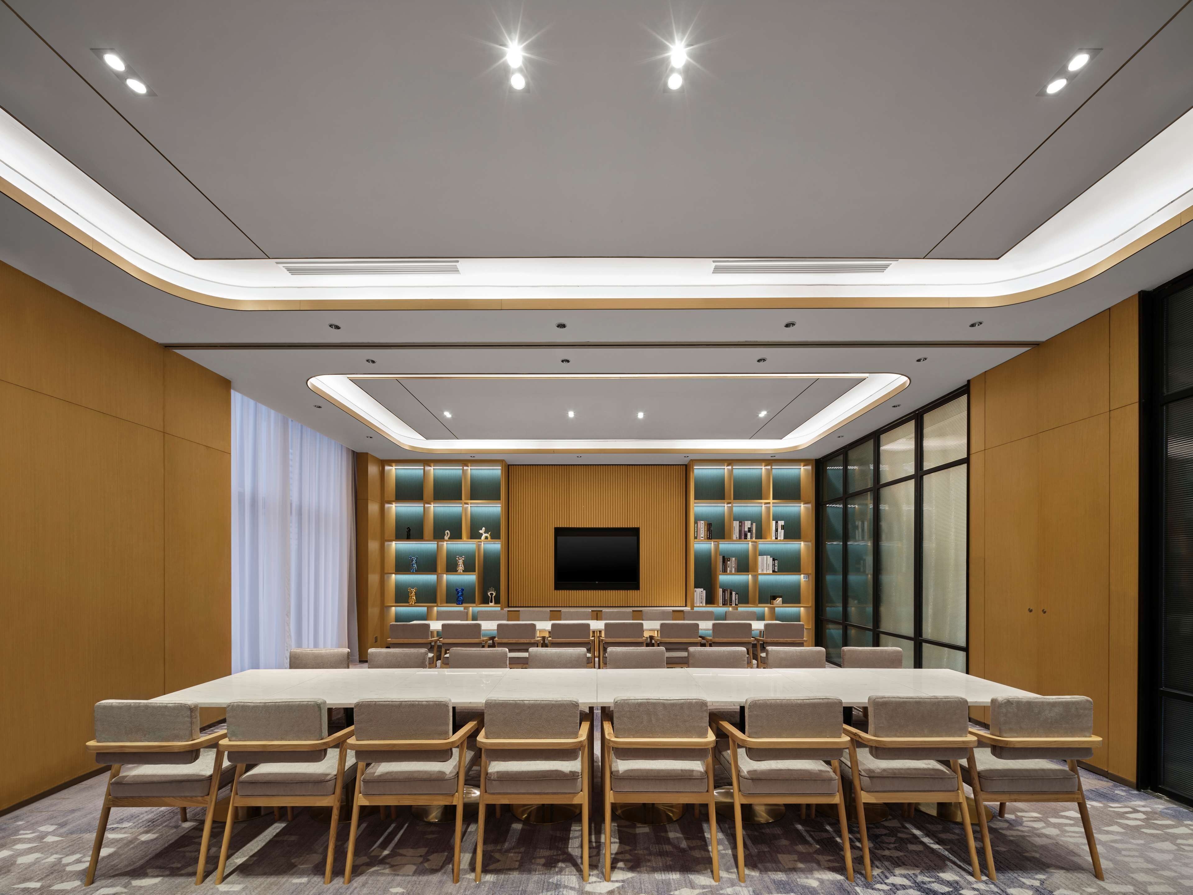Un salón de conferencias con una larga mesa, sillas, una televisión y estanterías.
