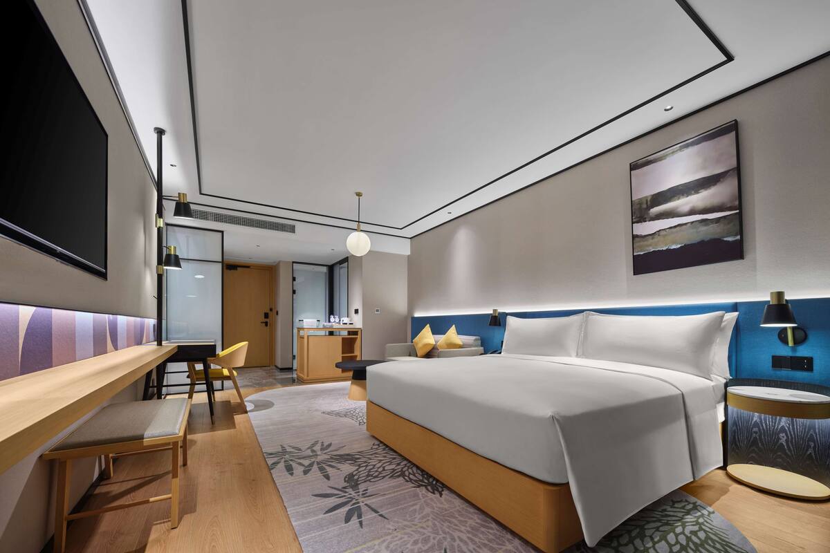 Una habitación de hotel moderna con una cama grande, un escritorio, una silla y una pequeña kitchenette.