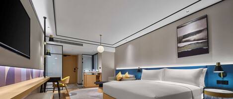 Una habitación de hotel moderna con una cama grande, un escritorio, una silla y una pequeña kitchenette.