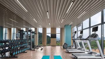 Academia com esteiras, halteres e aparelhos de musculação, janelas amplas com vista para as montanhas.